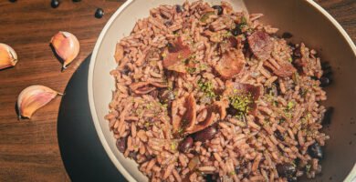 Un bol con arroz congrí en una mesa de madera decorada con ajos y frijoles negros