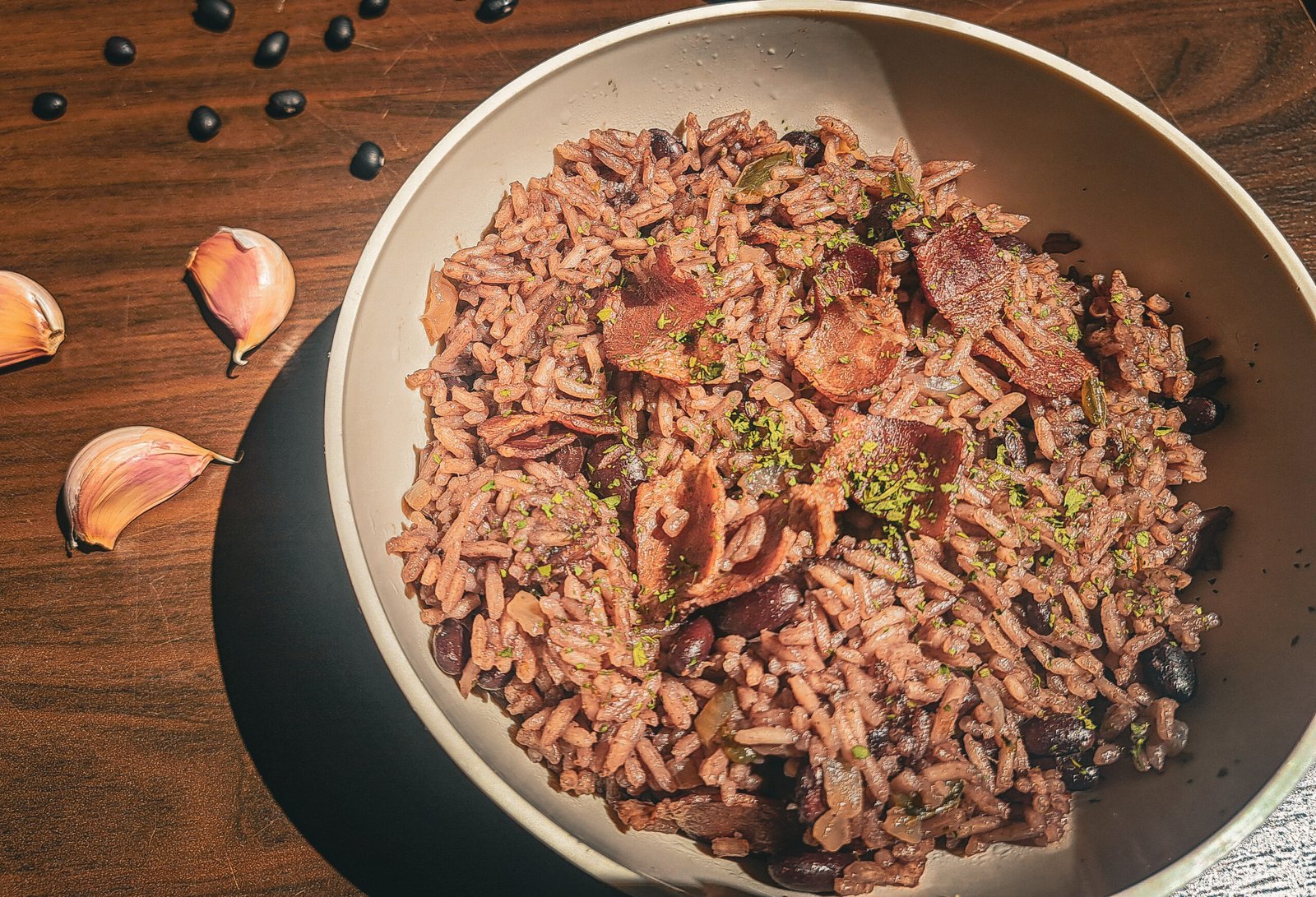 Un bol con arroz congrí en una mesa de madera decorada con ajos y frijoles negros